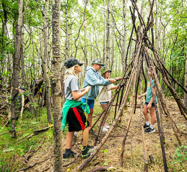 Group of campers learning how to built a wilderness shelter out of sticks v2