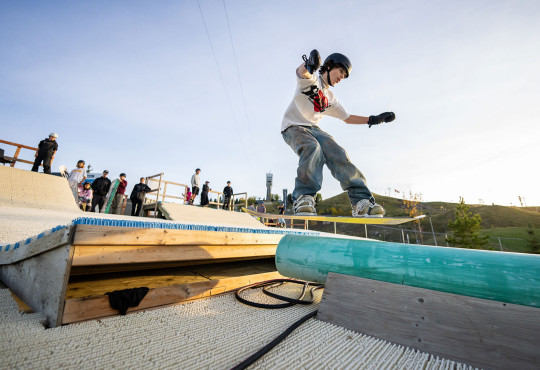 Summer camper on WinSports dryslope hitting a rail while on their snowboard v2